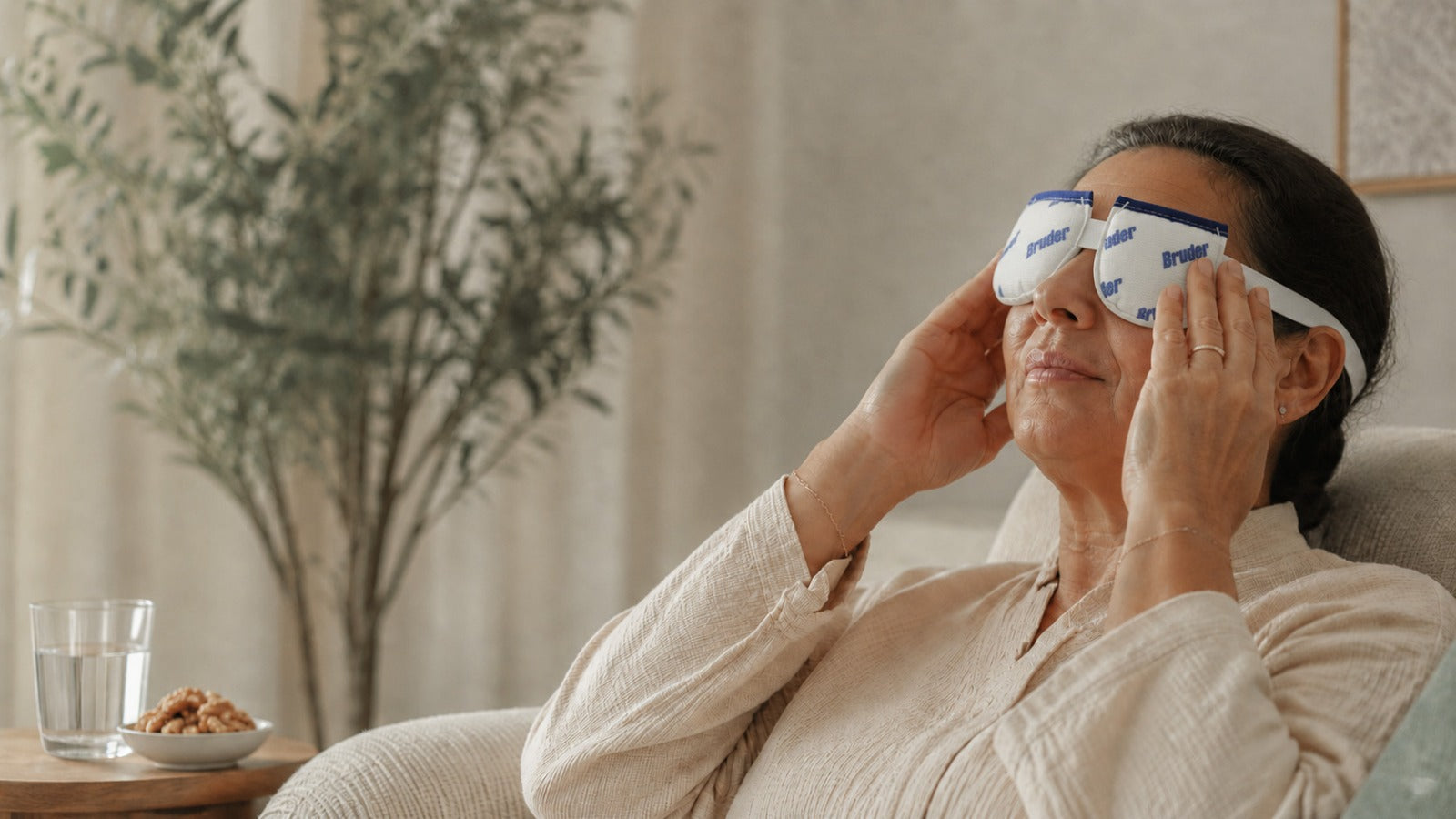 Midlife woman using a warm eye compress in a serene setting with water and omega-rich walnuts nearby.