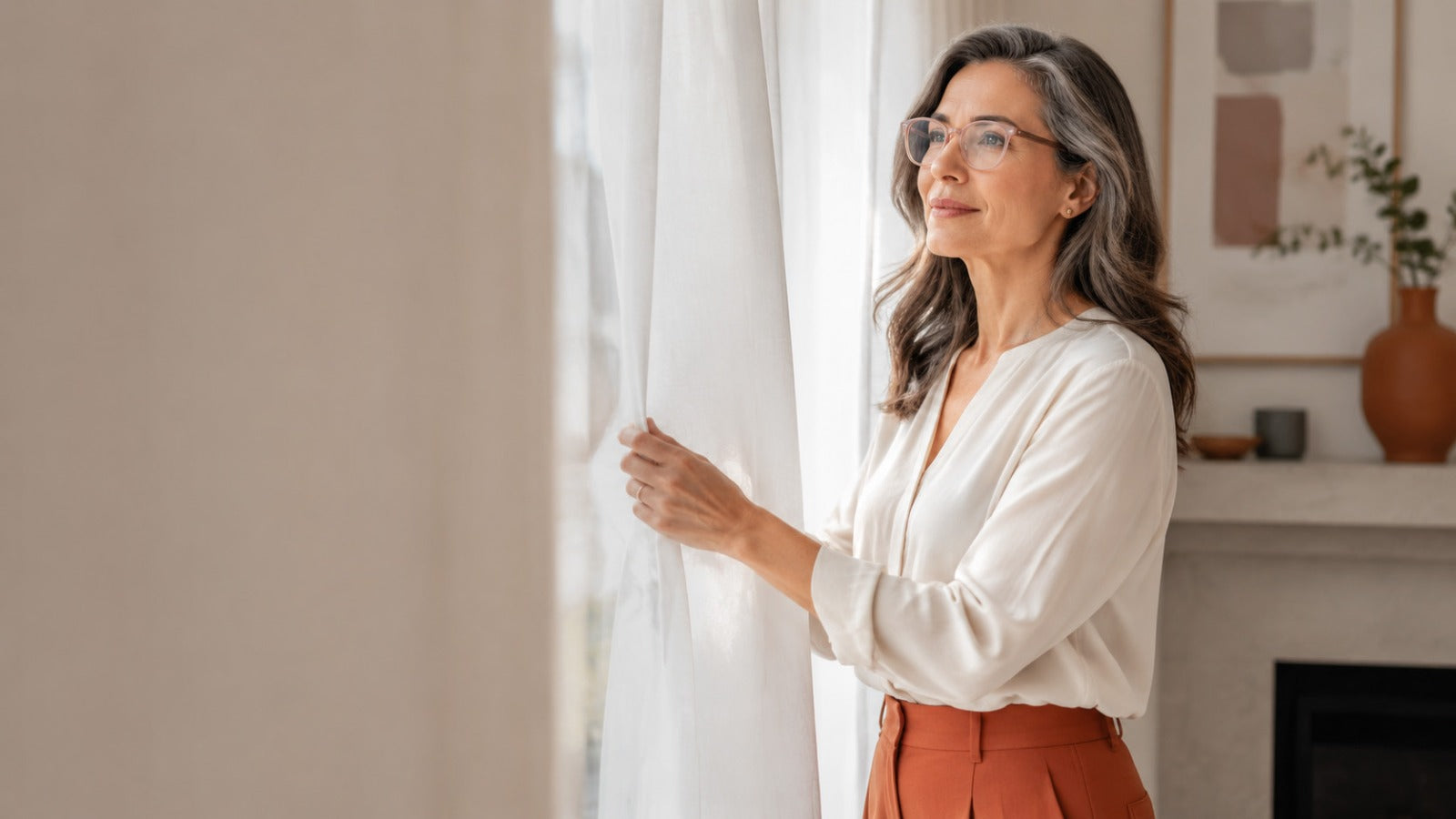 Woman managing bright indoor light comfortably with sheer curtains and subtle precision-tinted glasses.