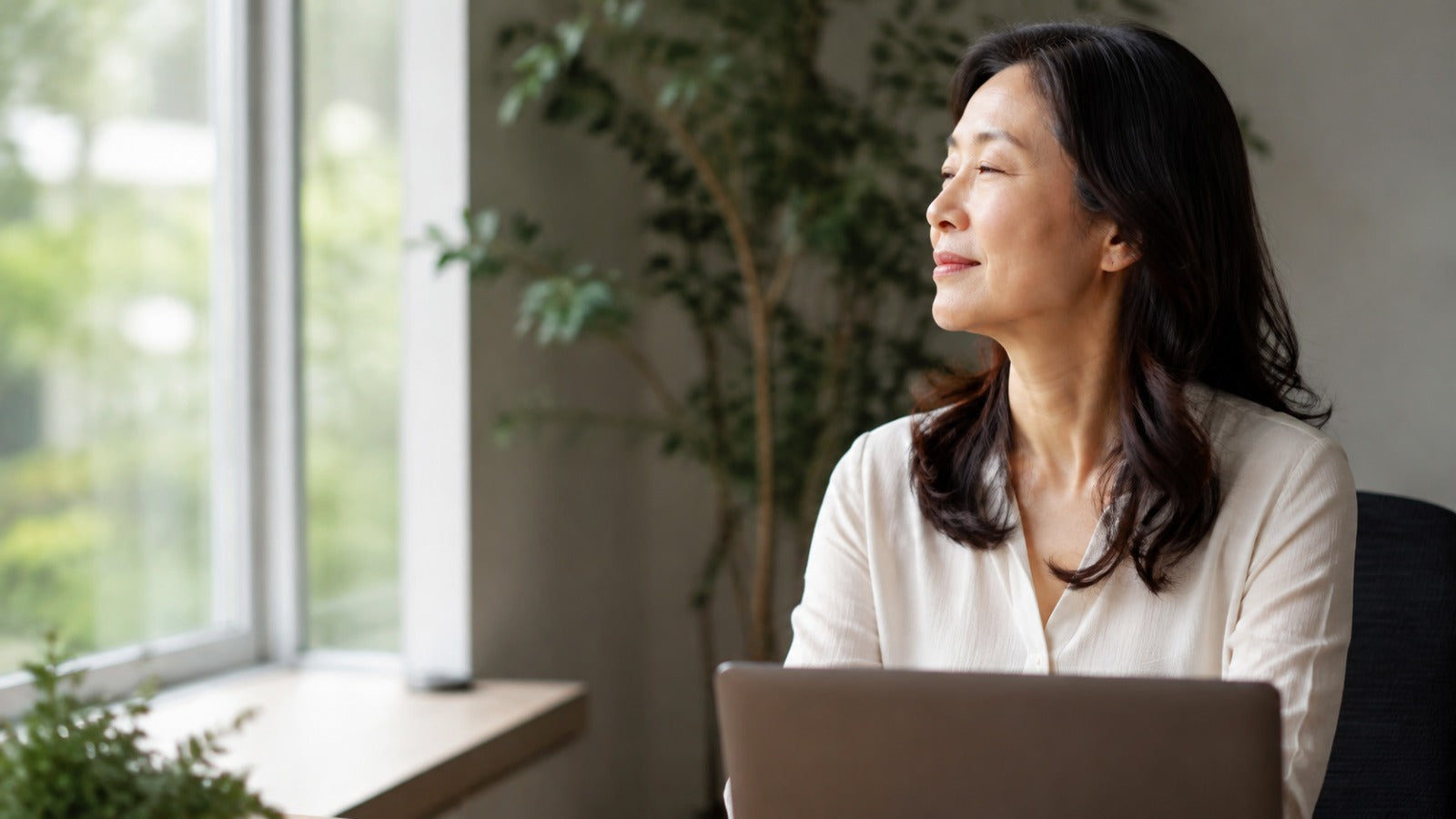 Professional Asian woman in her 50s taking a distanceviewing break from her laptop using the 20-20-20 rule